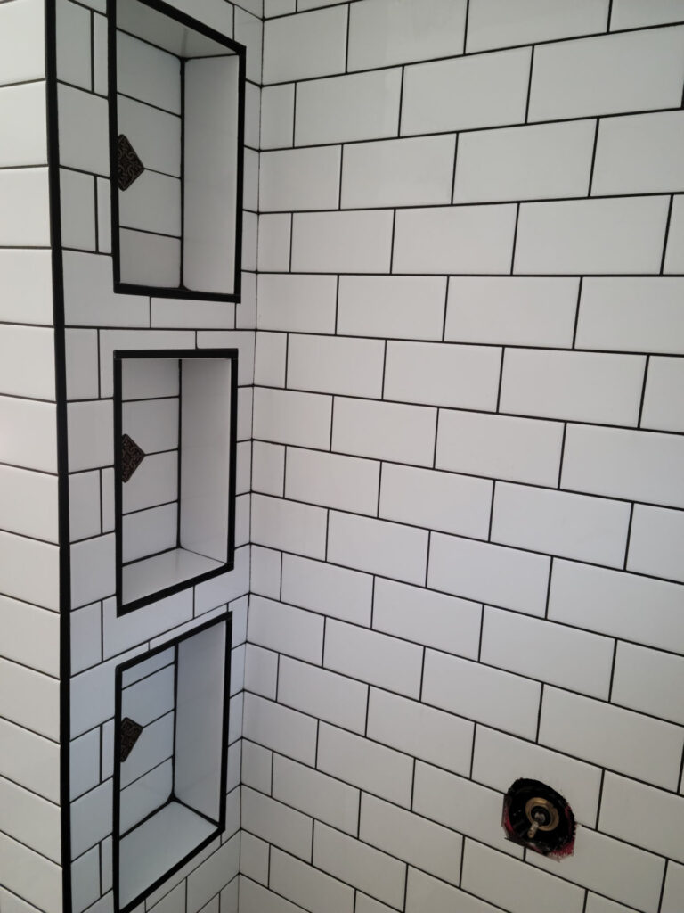White subway tile shower wall with black grout, three built-in rectangular niches on the left, and a pipe fitting on the right side—perfect inspiration for your next bathroom remodel in Phoenix.