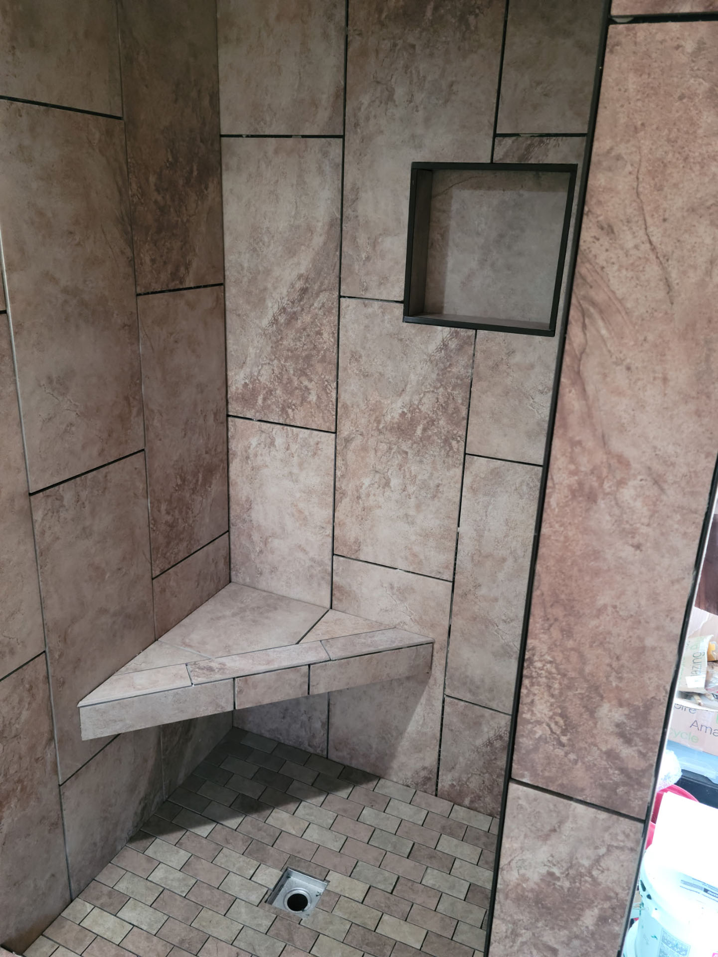 Shower with brown tiled walls, a built-in corner bench, a recessed shelf, and small square floor tiles with a central drain—perfect inspiration for your next bathroom remodel in Phoenix.